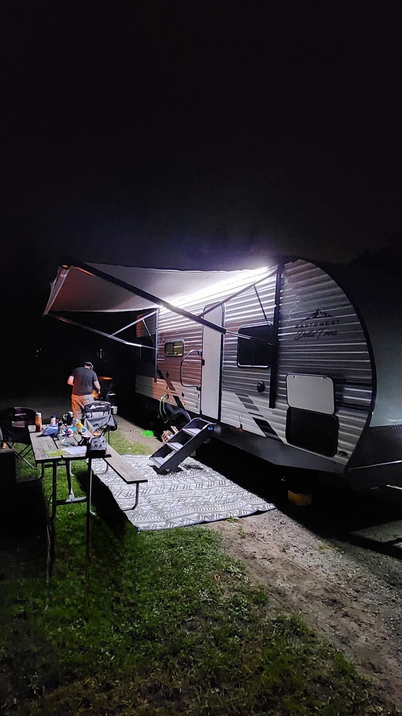 Travel trailer set up at night with the awning out, string lights on, and a picnic table beside it
