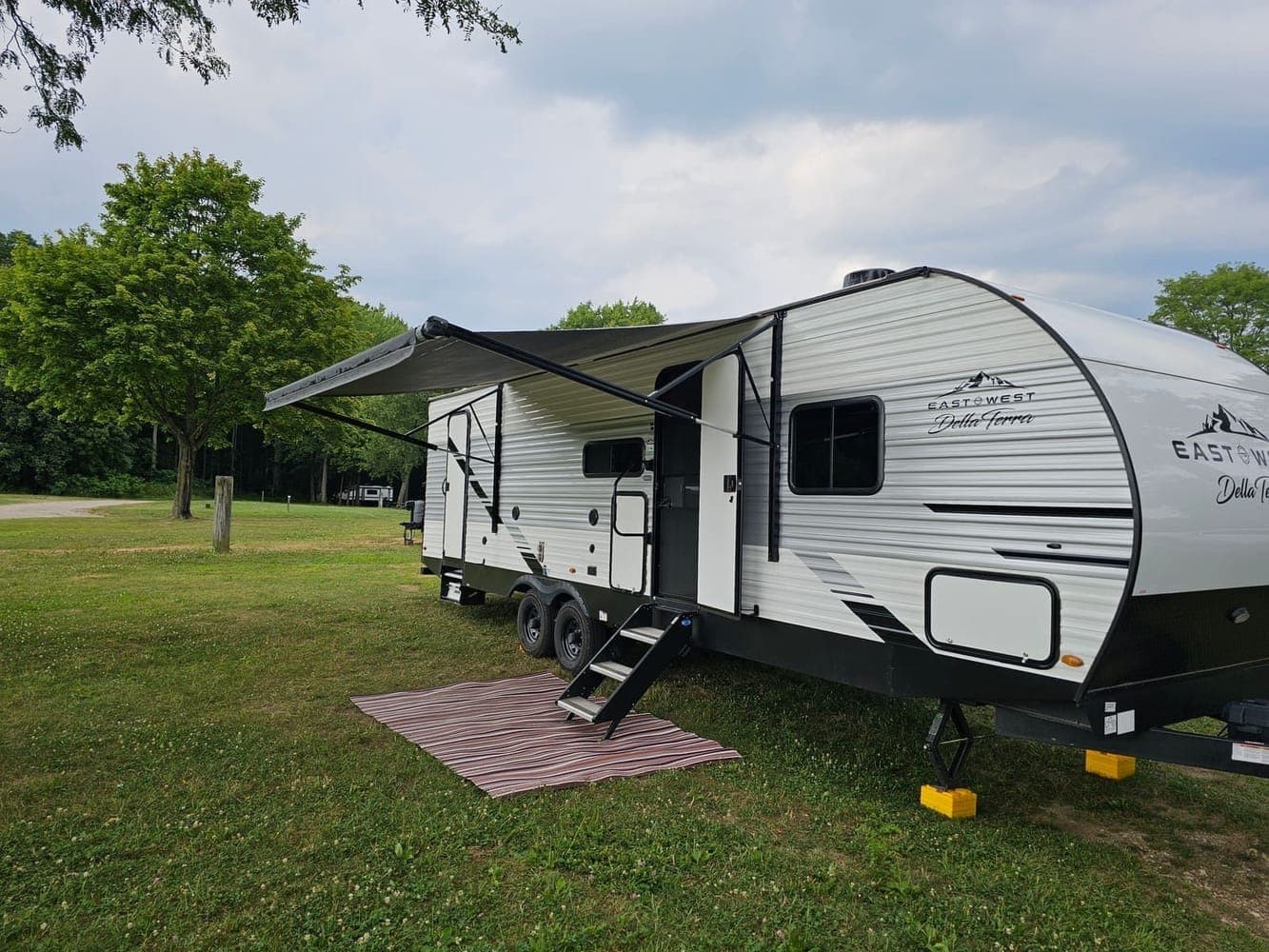 Travel trailer backed into a wooded campsite with leveling blocks under the frame and the awning extended