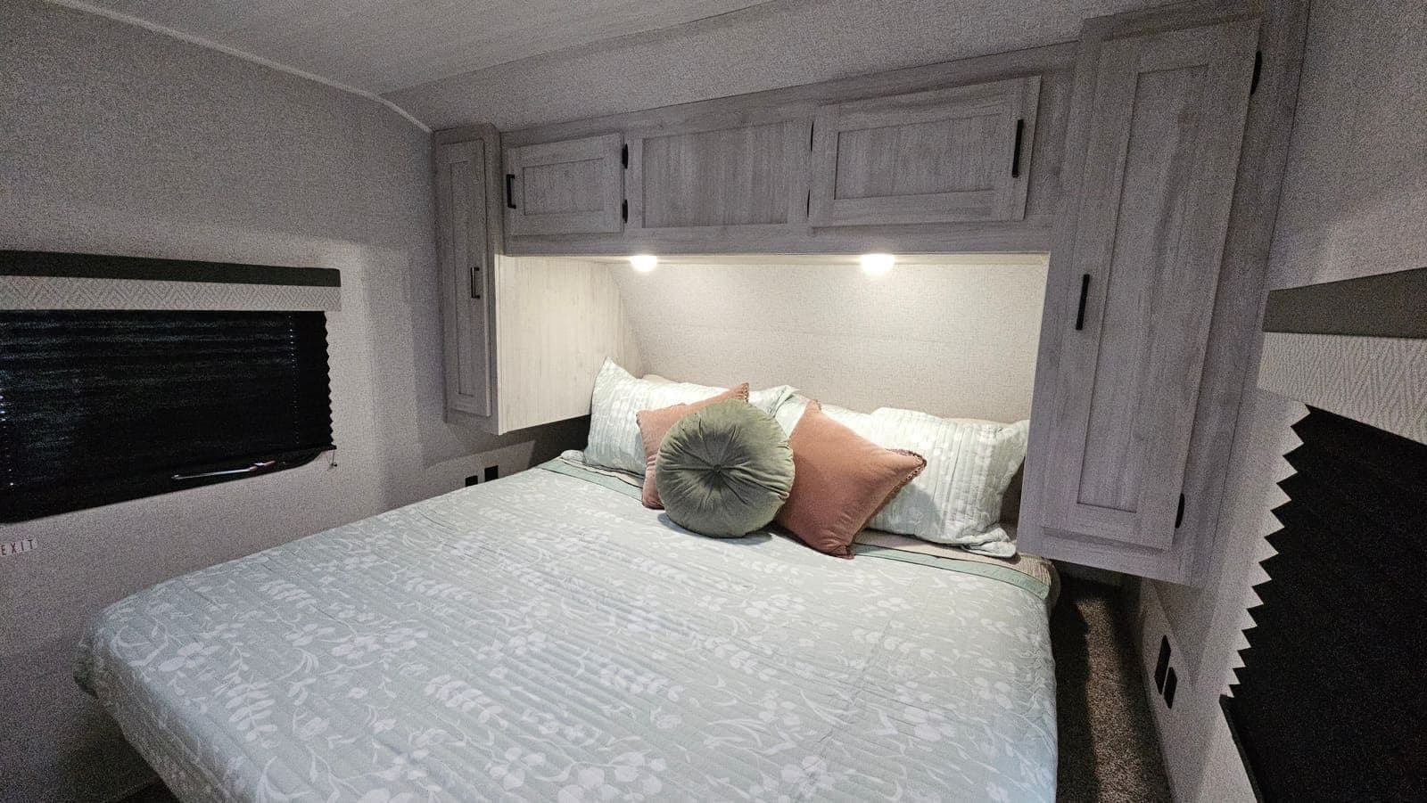 Made-up bed inside a Wanderous camper with pillows, overhead cabinets, and reading lights on