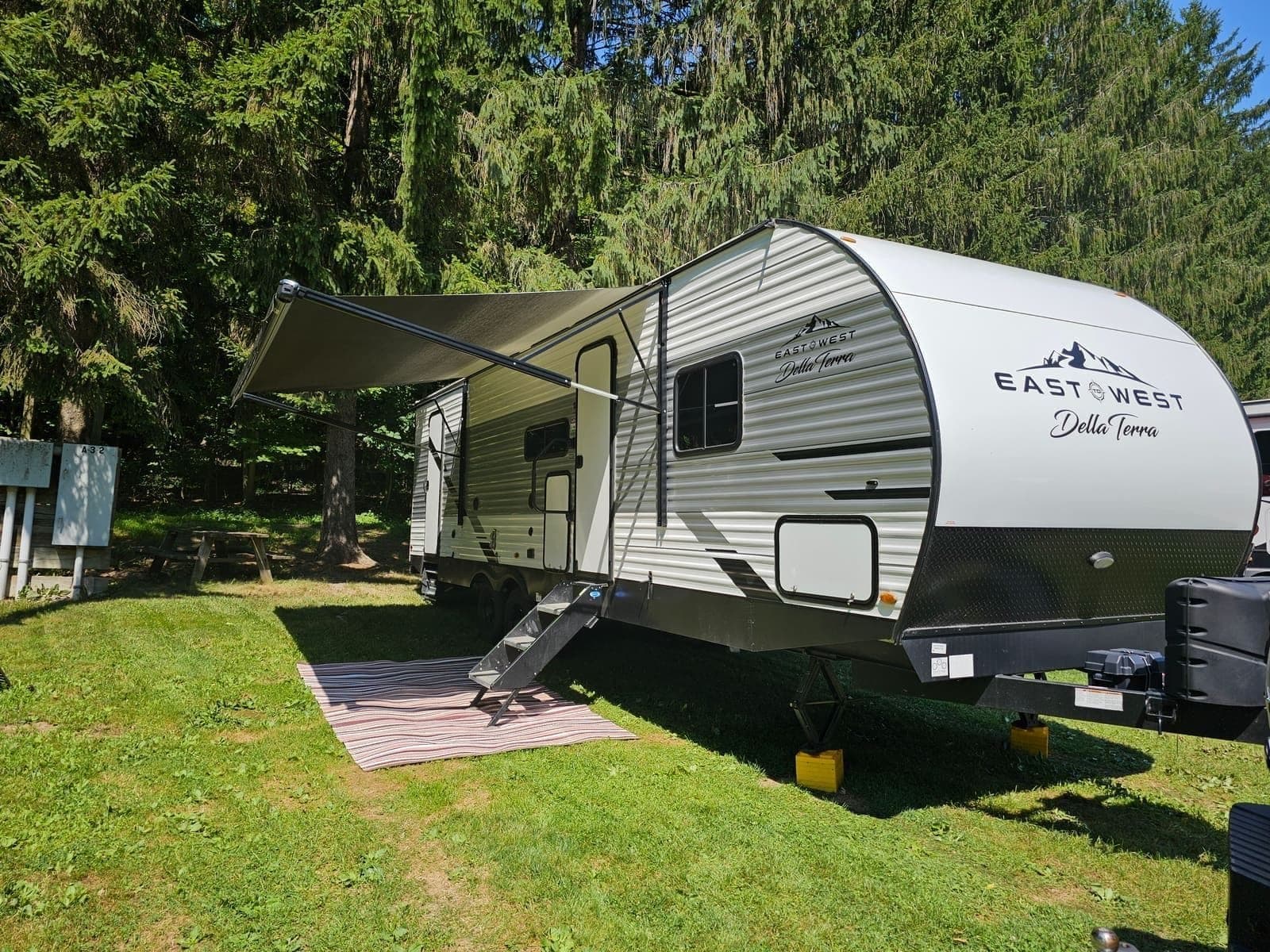 Travel trailer parked on grass with the awning out, an outdoor rug, and leveling blocks under the frame