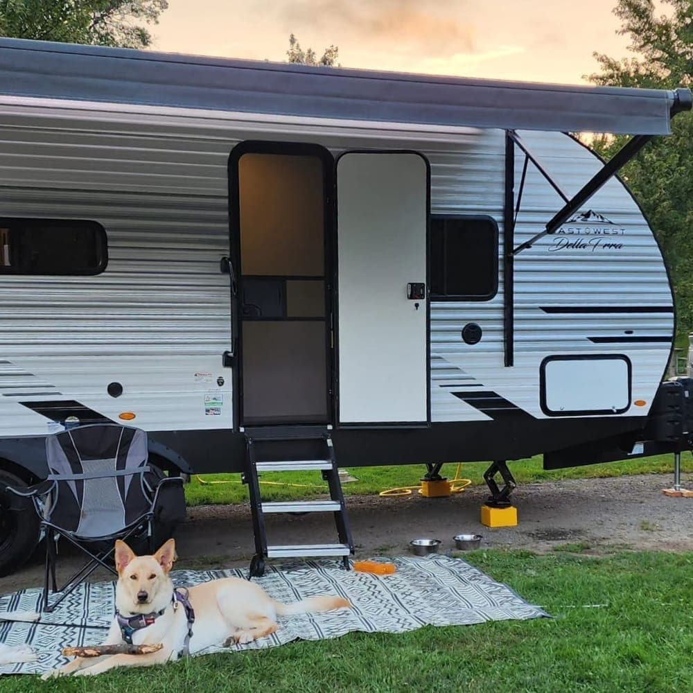 Travel trailer with camp chairs out front and a dog resting on the outdoor rug