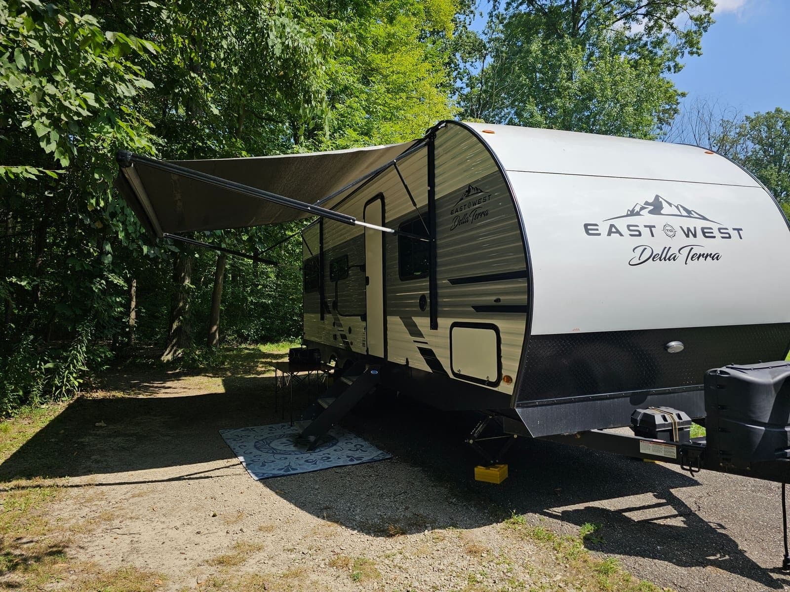 Travel trailer with the awning extended on a wooded gravel site
