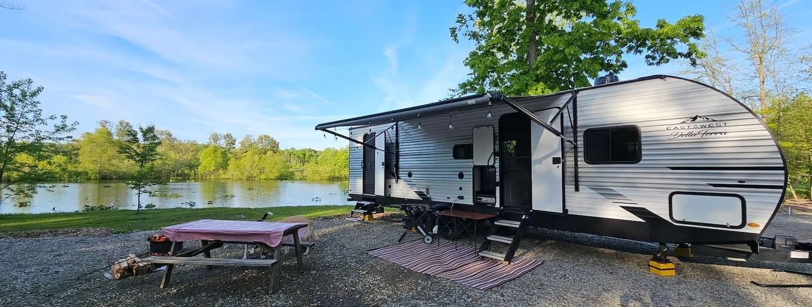 Travel trailer with awning out at a lakeside campsite, picnic table in front